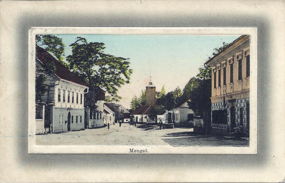 Fotografija: Veliki Mengeš okrog leta 1910 na razglednici, ki je bila odposlana na Dunaj: desno je Jenčičeva, levo Kančeva hiša, v sredini pa gasilski dom s stolpom.