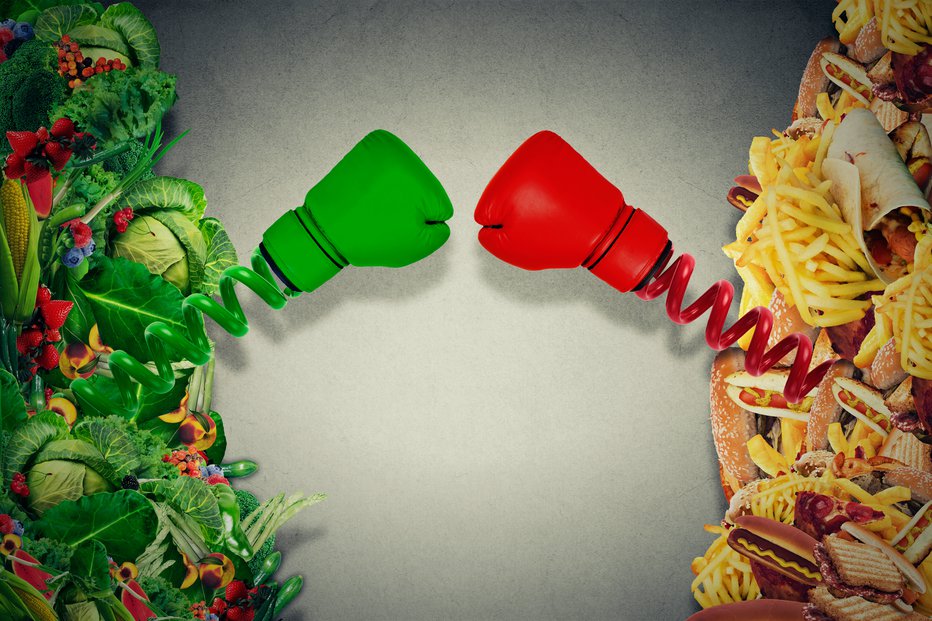 Fotografija: Vegetarian food fighting unhealthy junk food with boxing gloves punching each other. Diet battle nutrition concept.