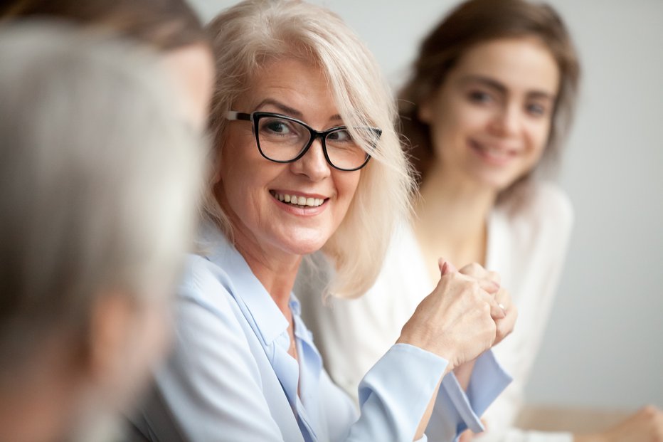 Fotografija: Smiling aged businesswoman in glasses looking at colleague at team meeting, happy attentive female team leader listening to new project idea, coach mentor teacher excited by interesting discussion FOTO: Fizkes Getty Images/istockphoto