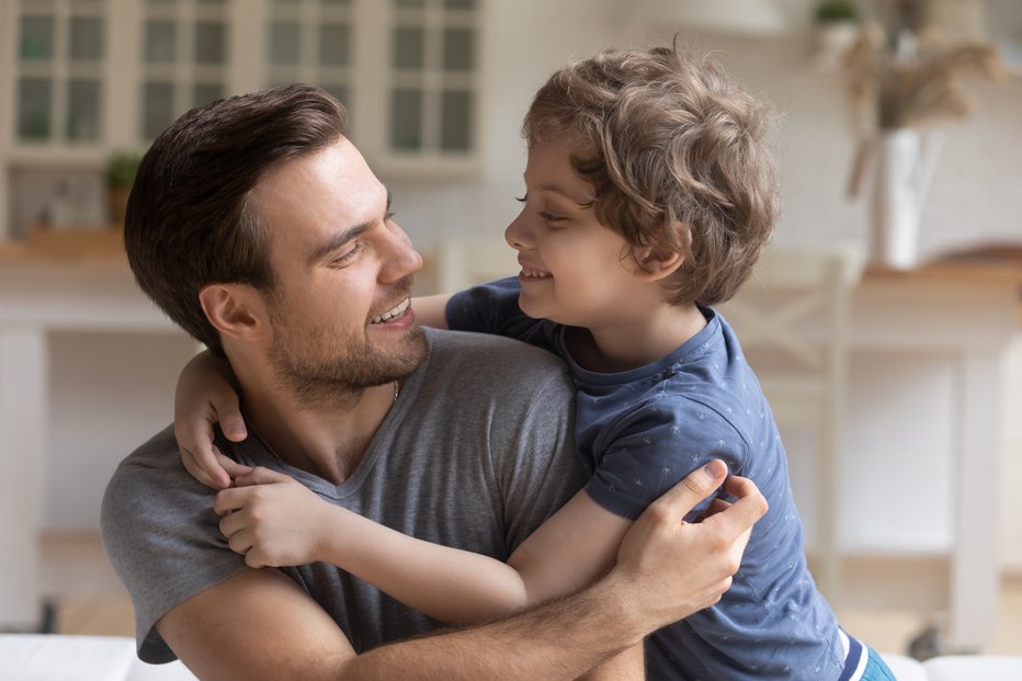 Fotografija: Loving dad caressing touching child sitting on sofa at home, happy daddy and little kid boy hugging having fun playing enjoy funny activities, good time together, father and son warm relations concept