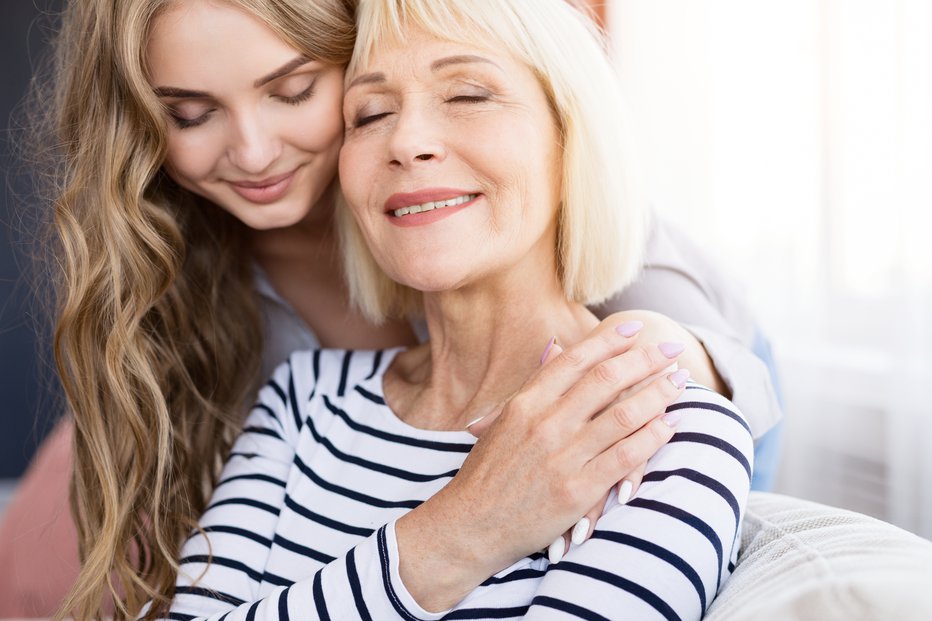 Fotografija: Cute young daughter embracing her mother with love, sitting on sofa at home