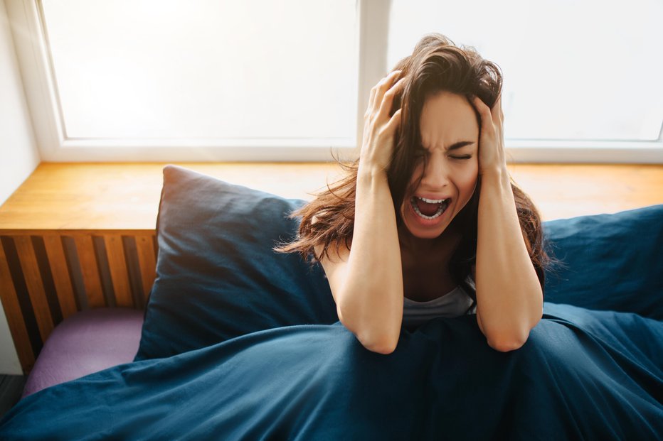 Fotografija: Young beautiful woman in morning bed at home. Sit and hold hands on head. Scream because of pain and stress. Depression and annoying condition