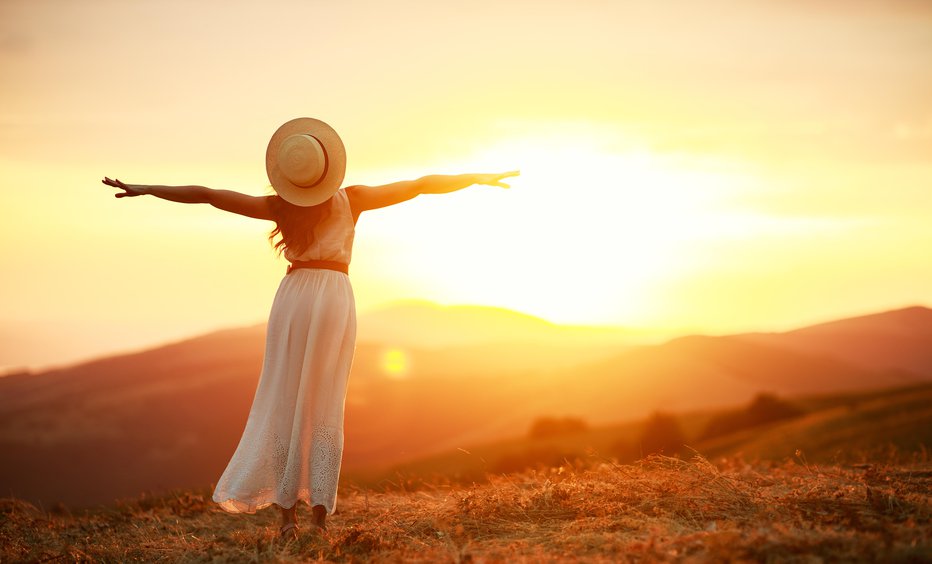 Fotografija: Happy woman standing with her back on the sunset in nature in summer with open hands