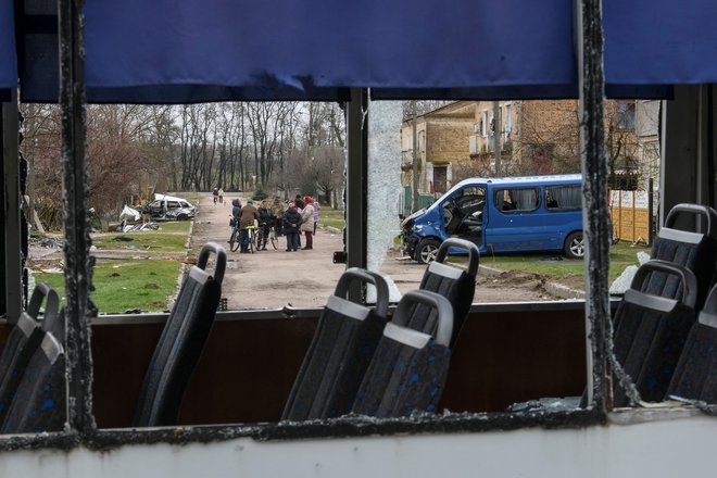 Domačini se zbirajo na ulici ob vozilih, uničenih med rusko invazijo, v vasi Jagidne. FOTO: Stringer/Reuters
