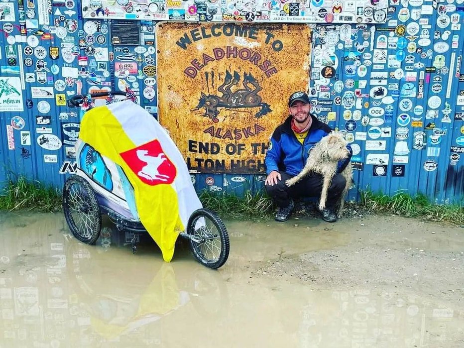 Fotografija: Oliver Tič ob tabli, ki je pomenila cilj njegove poti, na njegovem vozičku je zastava preljubih mu Slovenskih Konjic. FOTO: Dave Sner/Facebook
