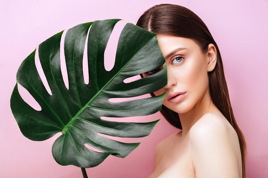 Fotografija: Beauty Woman with natural green palm leaf Portrait, model girl with perfect makeup, natural eyeshadows. Brunette Beautiful Fashion Model Girl Face. Skin care. Perfect Skin. On pink Background
