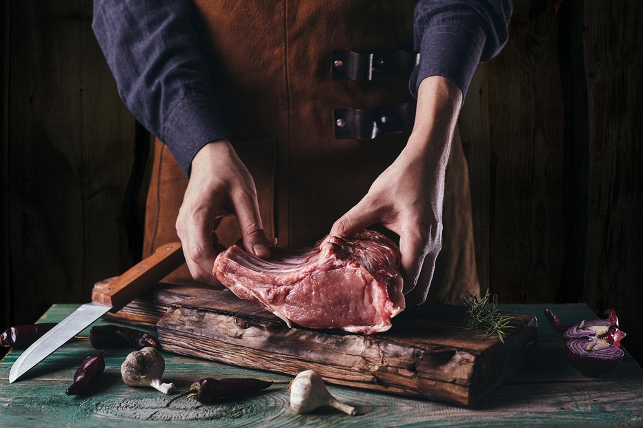 Fotografija: A guy in a leather apron is slicing raw meat. The butcher cuts the pork ribs. Meat with bone on a wooden cutting board. FOTO: Serhii Opikanets Getty Images/istockphoto