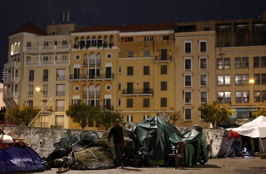 Fotografija: Razseljenec se v dežju sprehaja pred šotorom na osrednjem Trgu mučencev v Bejrutu, kjer prenočujejo številne družine, ki bežijo pred nenehnimi izraelskimi napadi na jugu Bejruta, Libanon, 3. november 2024. FOTO: Mohamed Abd El Ghany Reuters