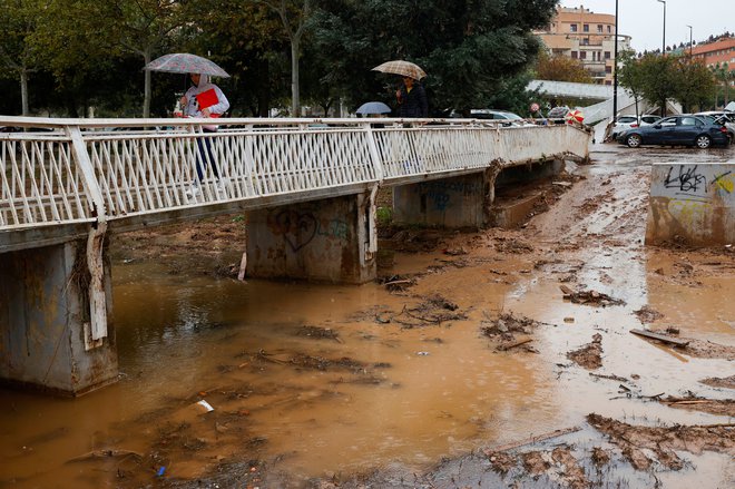 Družina prečka sotesko La Saleta, ki je poplavljena zaradi obilnega deževja v kraju Aldaia v španski Valencii, 13. novembra 2024. FOTO: Eva Manez Reuters