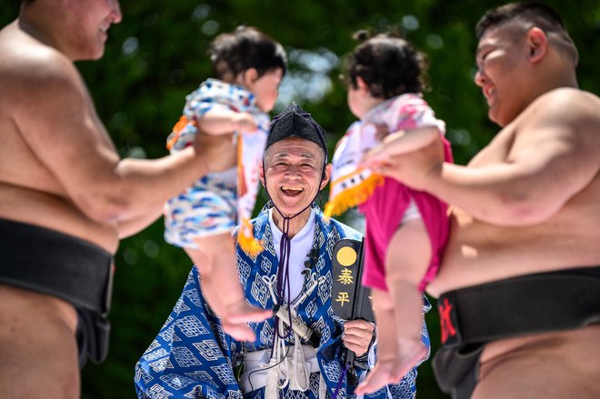 Sumoborca držita otroka pred začetkom turnirja v otroškem joku, zmaga tisti, ki drži glasnejšega; obred naj bi poskrbel za zdravje malčkov in odgnal zle duhove. FOTO: Philip Fong/AFP