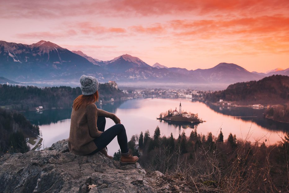 Fotografija: Travel Slovenia, Europe. Woman looking on Bled Lake with Island, Castle and Alps Mountain on background. Top view. Bled Lake one of most amazing tourist attractions. Sunset winter nature landscape.