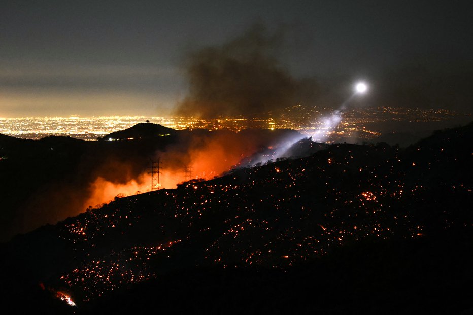 Fotografija: Svetloba gasilskega helikopterja osvetljuje tleče pobočje, ko se širi požar Palisades. Ta, največji od losangeleških požarov, se je 11. januarja razširil proti prej nedotaknjenim soseskam, zaradi česar so bile potrebne nove evakuacije. FOTO: Patrick T. Fallon Afp